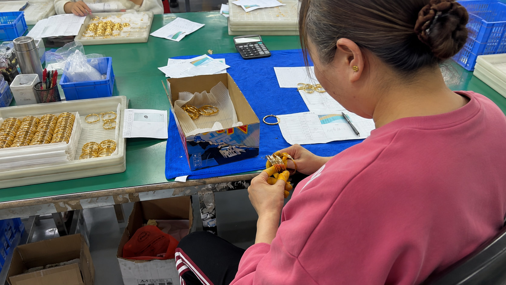 Worker inspecting gold-tone stainless steel bangles during jewelry quality control
