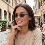 Female model wearing translucent brown oval sunglasses sitting at a street-side café, casual lifestyle fashion look