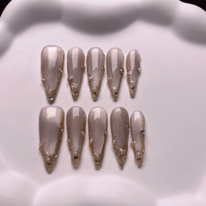 A Set of 10 Handmade Press-On Nails That Can Be Reused Multiple Times, Featuring Unique Stiletto Shapes in Champagne And Golden French Styles, Adorned with Luxurious Crystals And Shiny Pearls.